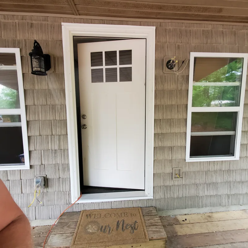 Close view of a white painted front door with a four-pane window and white trim on grey shake siding