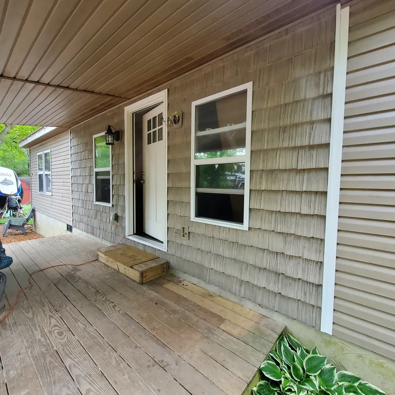 Covered porch with grey shake siding, a white painted entry door with a window, white trim and a wood deck