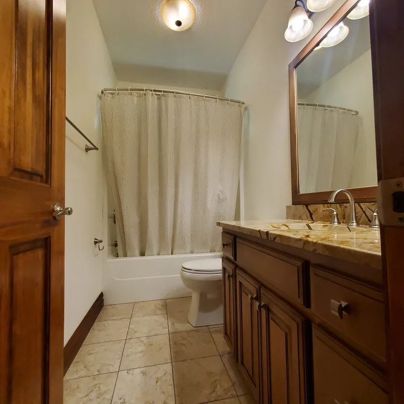 Bathroom with a wood vanity, granite top, tiled floor and painted white walls
