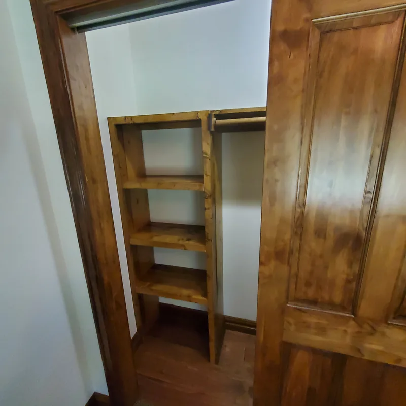 Walk-in closet with stained wood shelving and a clothes rod against painted white walls