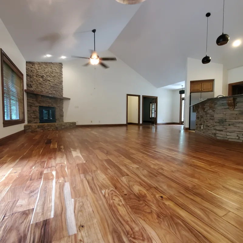 Great room with a stacked-stone fireplace, ceiling fan, hardwood floor and newly painted white walls and ceiling