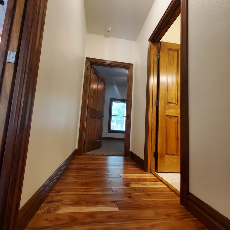 Hallway with stained wood doors and trim, hardwood floor and painted off-white walls