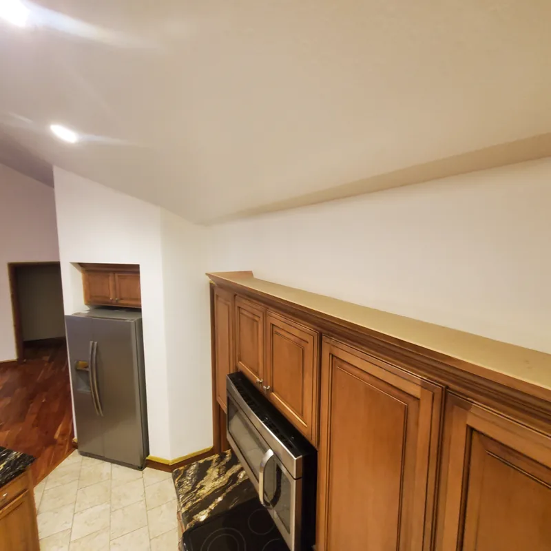 Kitchen corner with oak cabinets, a stainless refrigerator, and a freshly painted wall meeting a sloped ceiling