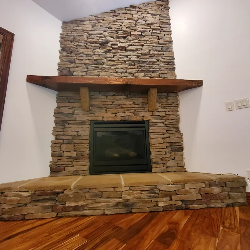 Stacked-stone fireplace with a rustic wood mantel against a freshly painted white wall
